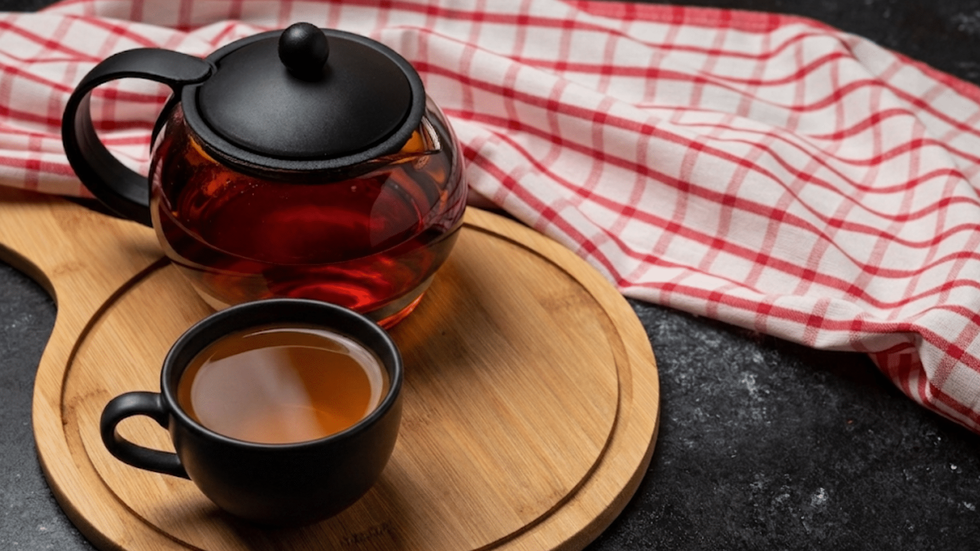 black teapot and matching teacup filled with freshly brewed earl grey tea on a wooden serving
