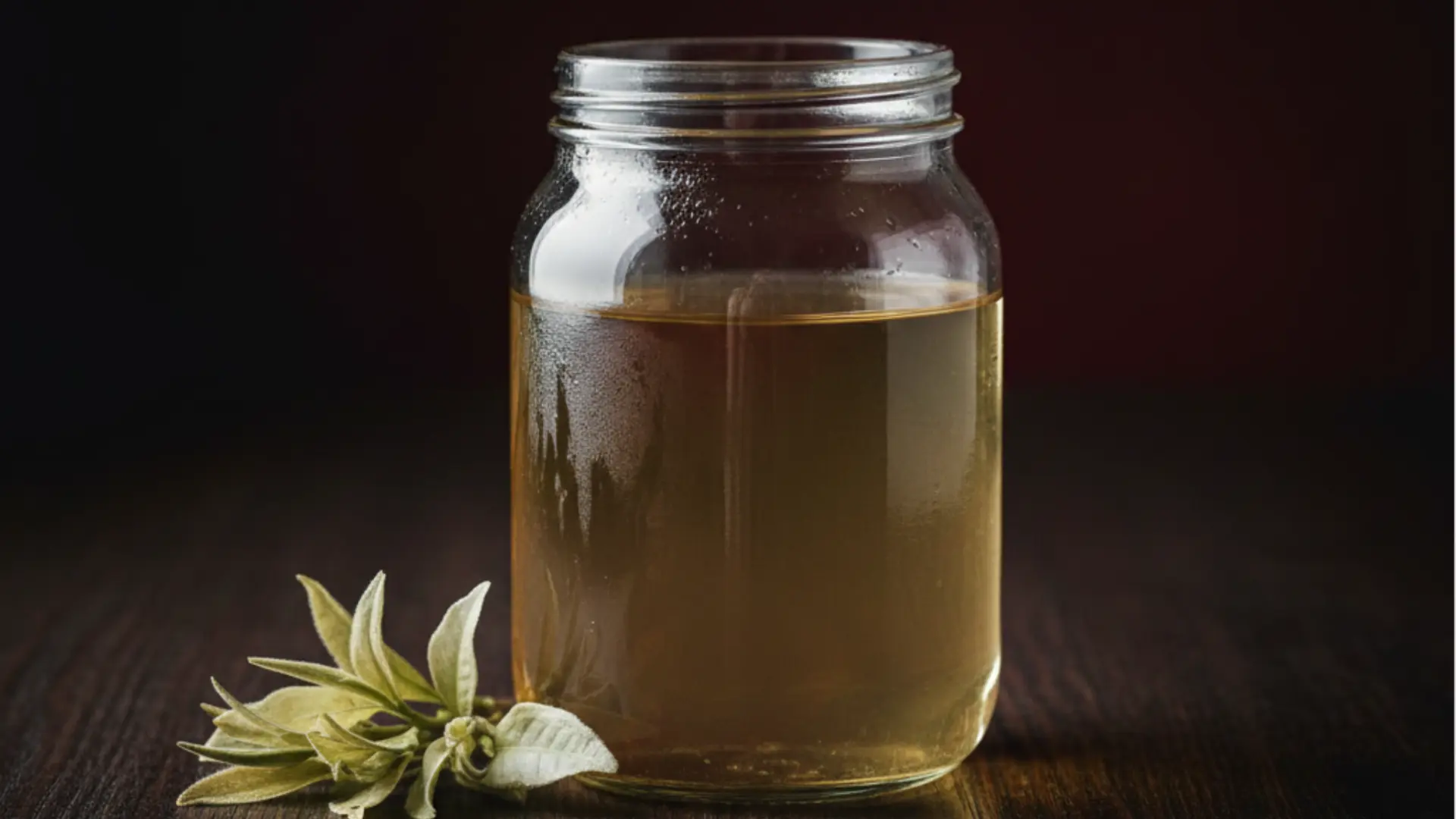 glass jar filled with amber cold-brew white tea sits on a dark wooden surface next to fresh tea leaves