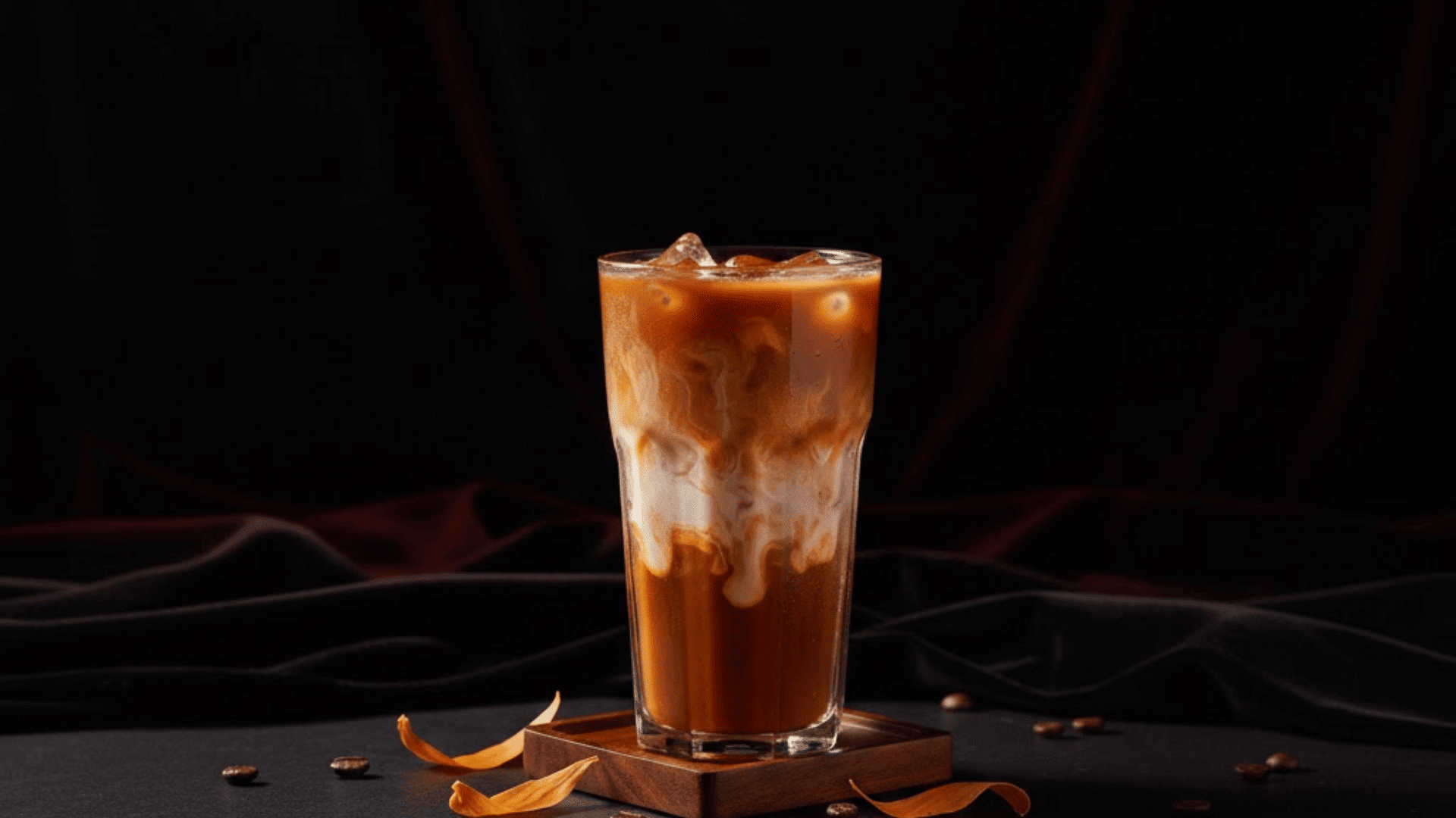 iced thai tea with milk swirls in tall glass on wooden coaster with scattered coffee beans on dark surface