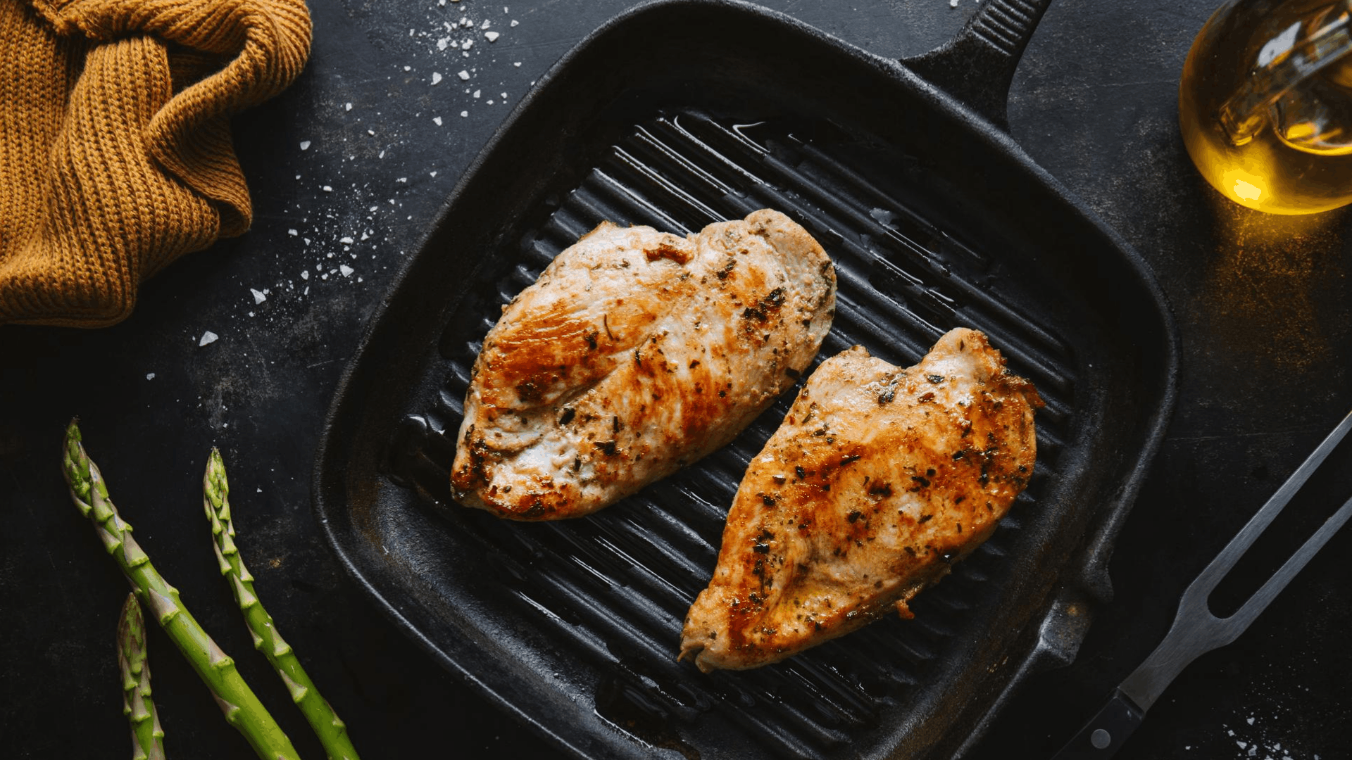 two grilled chicken breasts sesoned with herbs in a black cast Iron grill pan