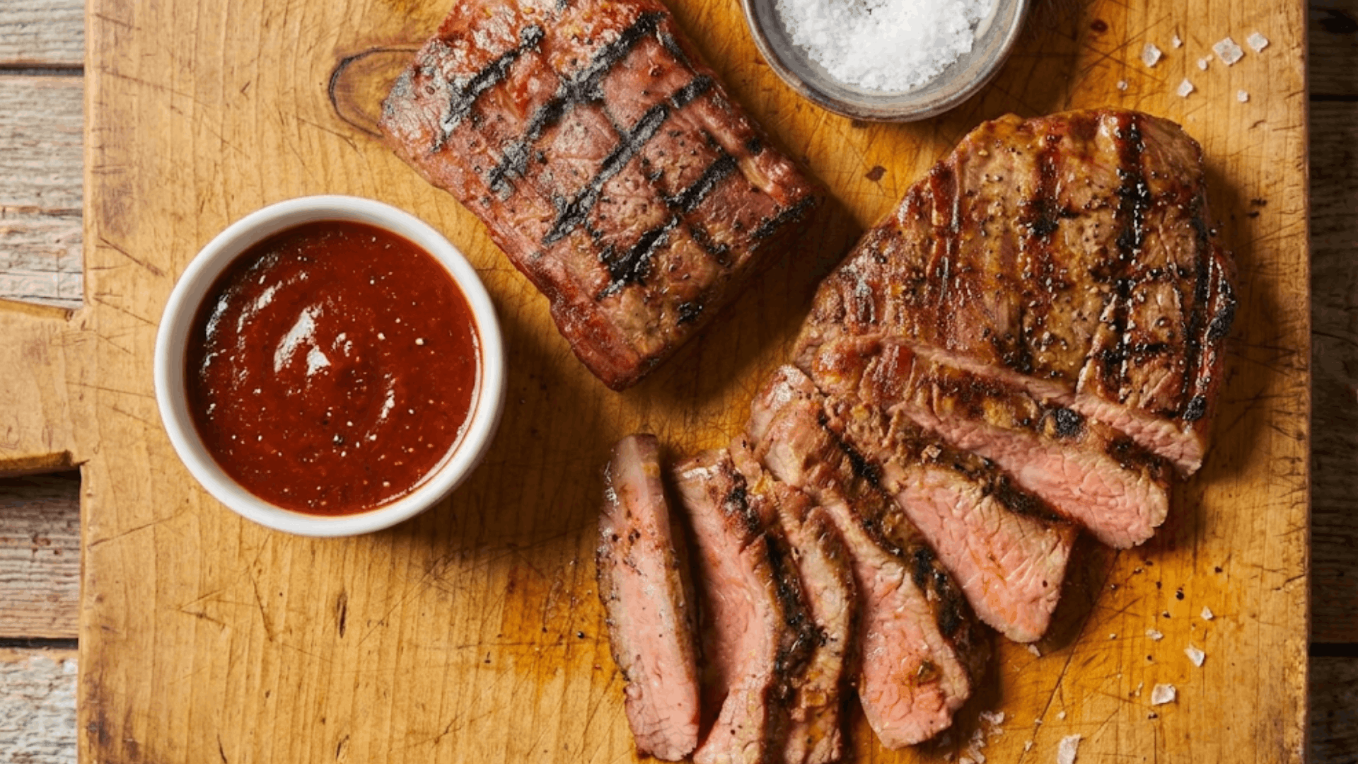 Grilled flank steak sliced on a wooden cutting board with dipping sauce and sea salt highlighting a juicy high protein lean beef cut