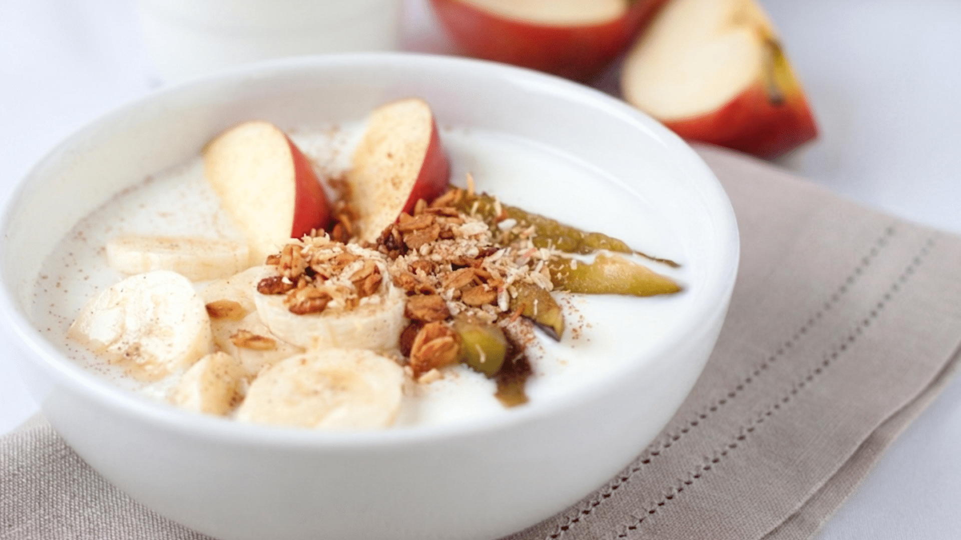 bowl of plain yogurt topped with banana slices apple slices granola and fruit served as a stomach friendly breakfast