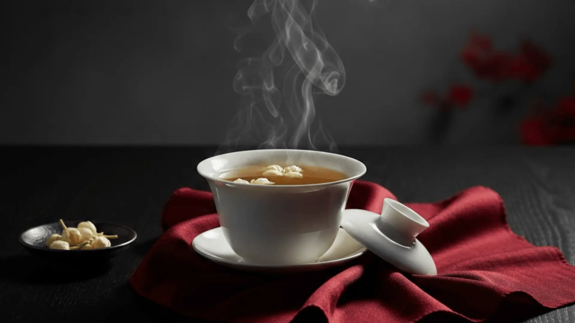 hot tea served in white cup placed on red fabric with steam rising against dark background creating cozy mood scene