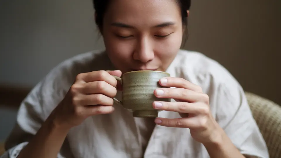 person holding a green tea cup while sitting calmly in soft indoor light for a hydration blog image