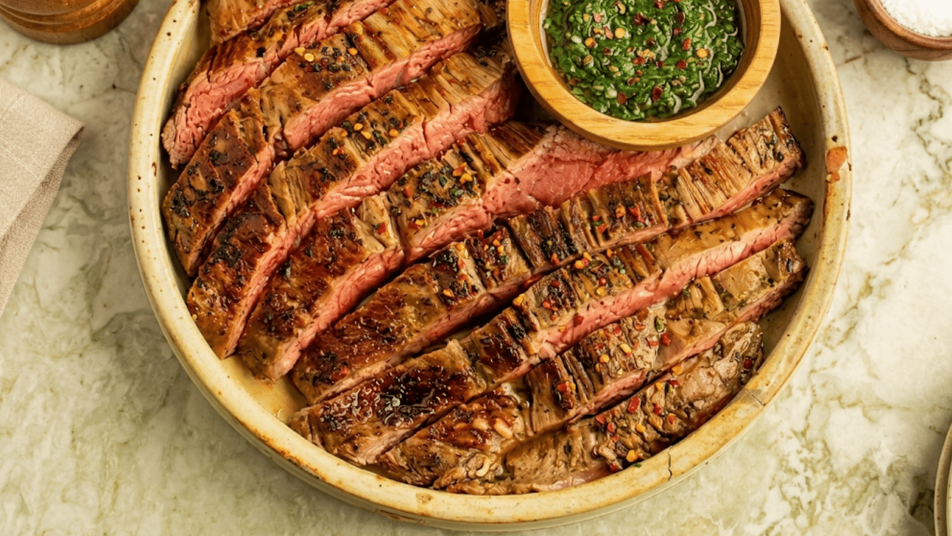 sliced medium rare flank steak served on a black slate board with grilled garlic tomato and fresh rosemary garnish