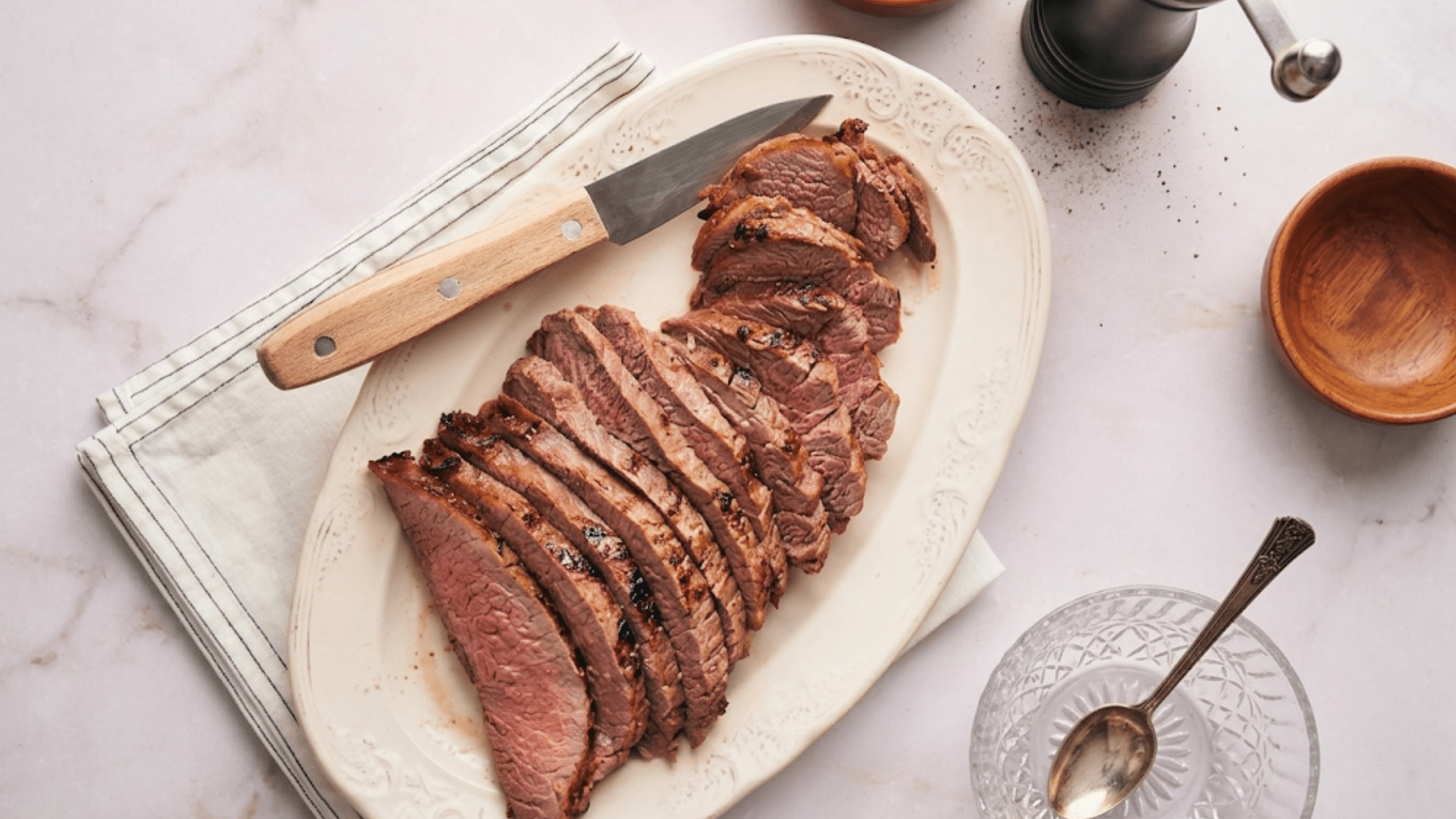 sliced medium rare flank steak served on a black slate board with grilled garlic tomato and fresh rosemary garnish