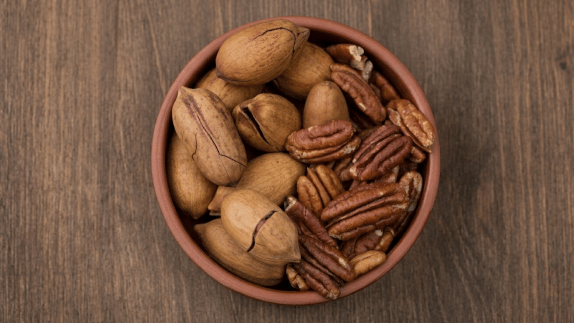top over view of pecans in a red bowl placed on a wooden table