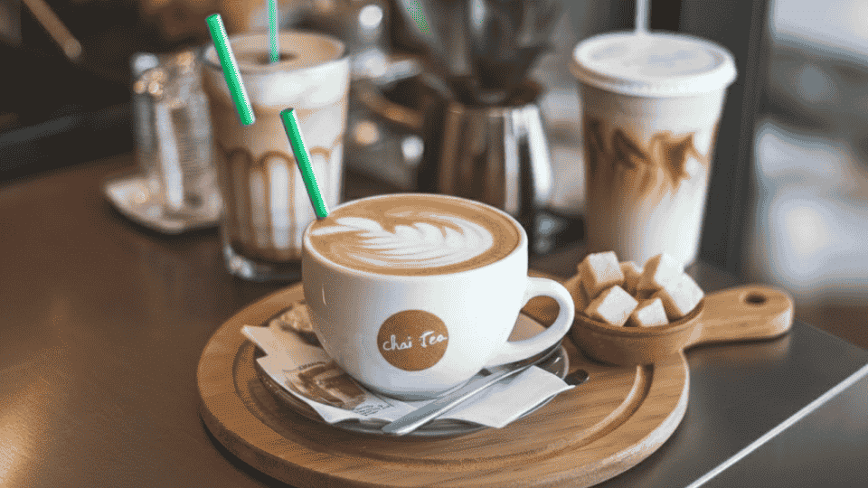 a chai tea latte with a green straw, sugar cubes, and a few other beverages on a table at a cafe in daytime