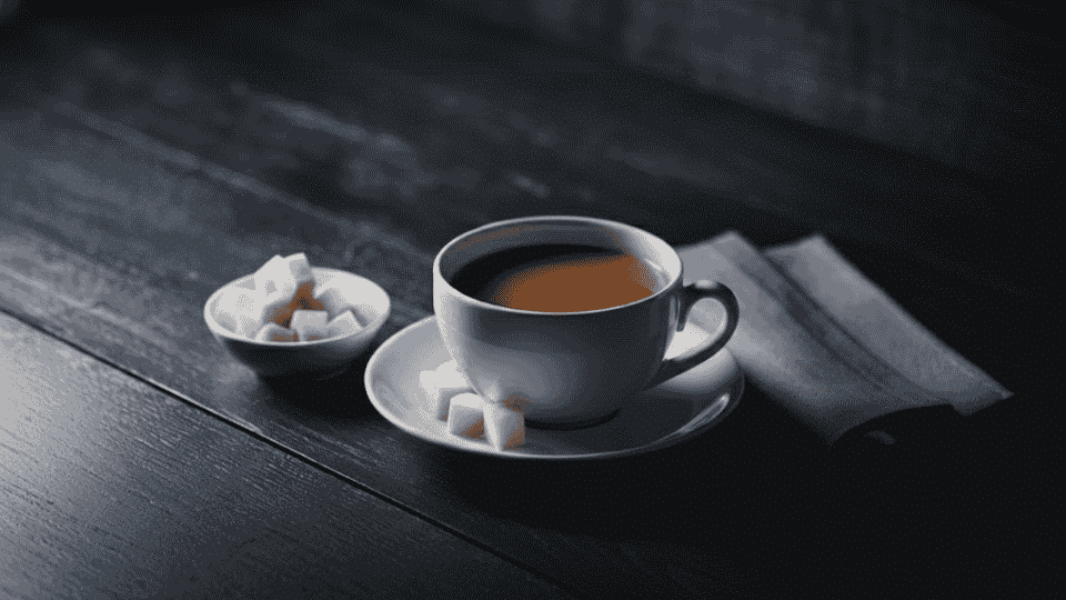 a cup of chai with a bowl of sugar cubes beside it, resting on a saucer, with a napkin on a dark table