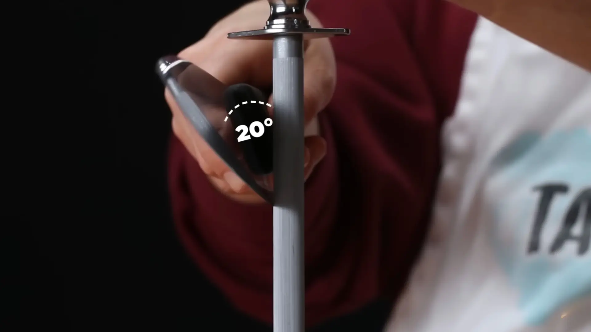 a person holds a kitchen knife at a angle against a honing steel to realign the blade's edge