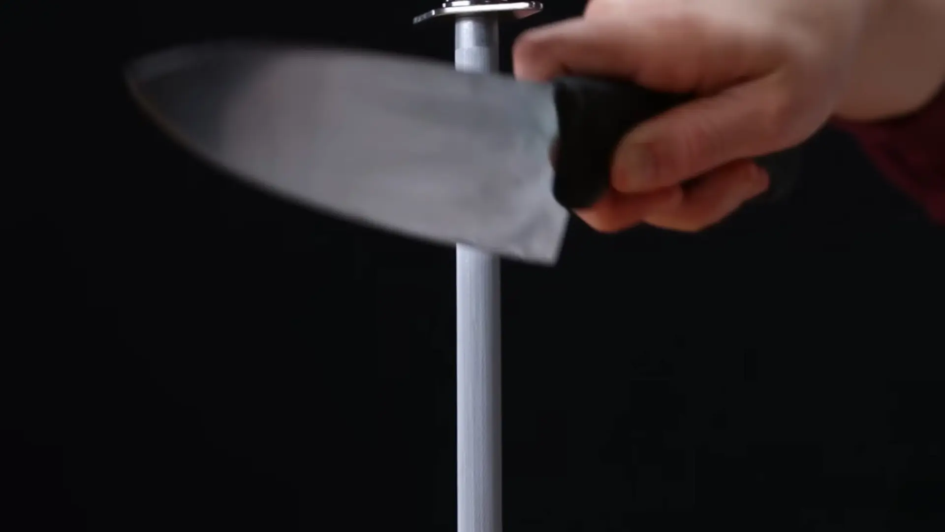 a person sweeps a chef's knife downward against a vertical honing steel to realign the blade's edge