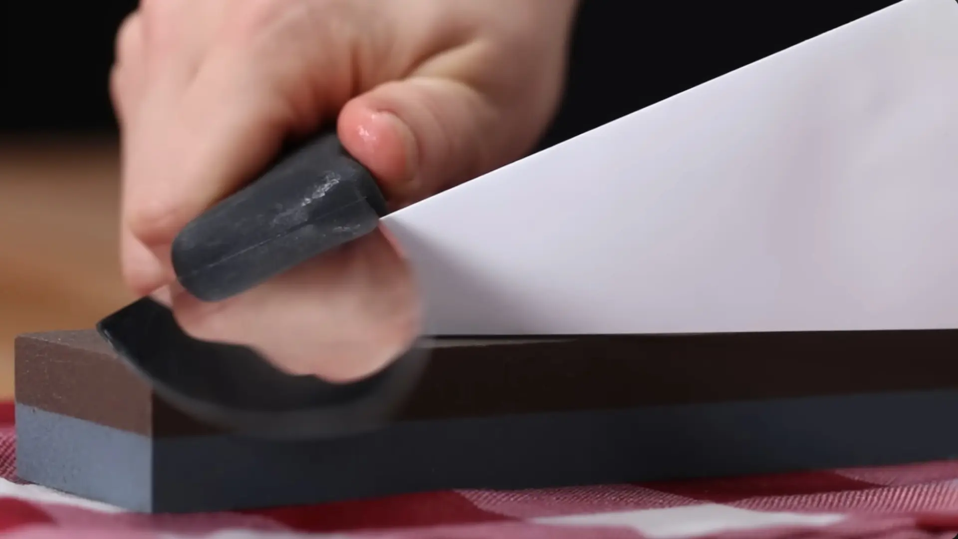 a person uses a paper guide to hold a knife at a angle while sharpening it on a whetstone