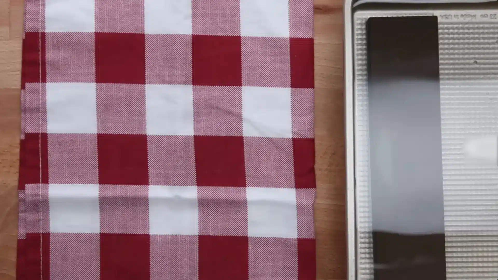 a red and white checkered kitchen towel lies next to a whetstone on a baking sheet