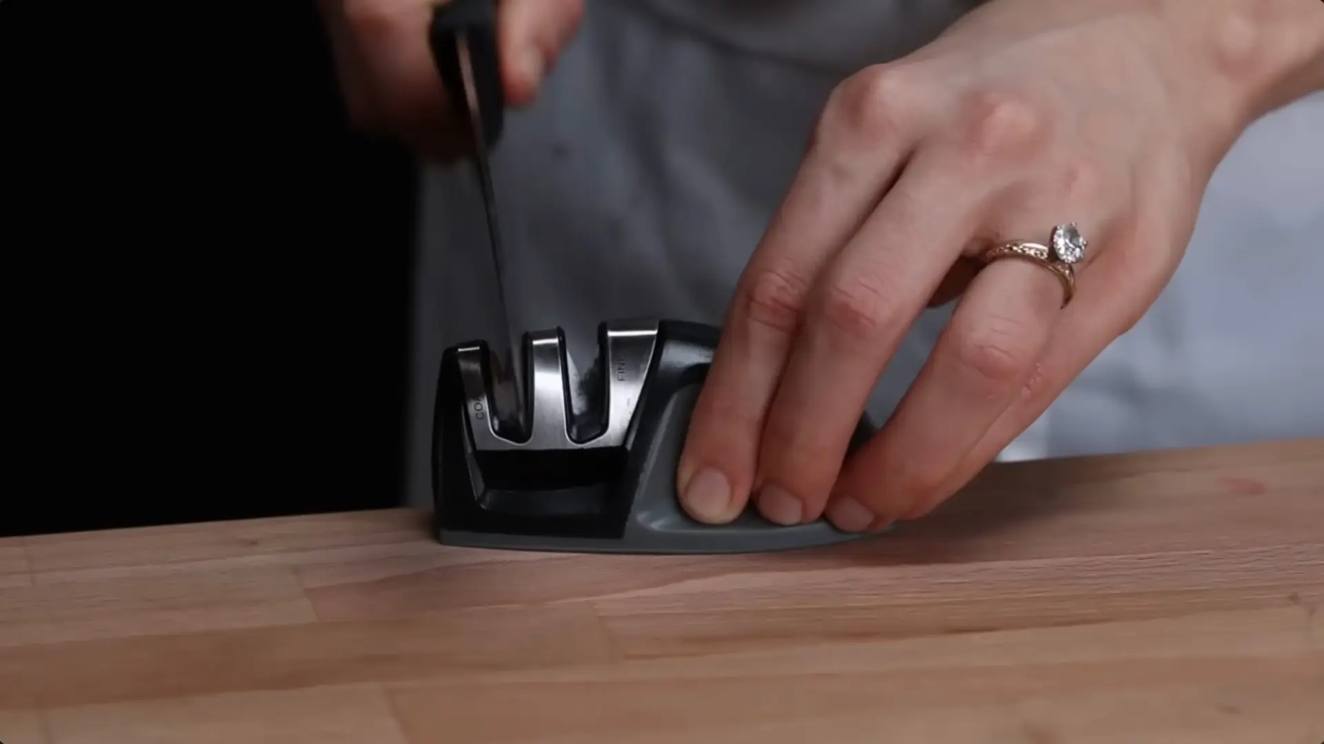 a top-down view of a grey and black pull-through knife sharpener on a light wood surface