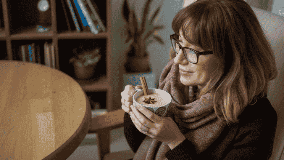 a woman is enjoying a warm cup of chai, holding it with a smile, cinnamon and star anise in the cup