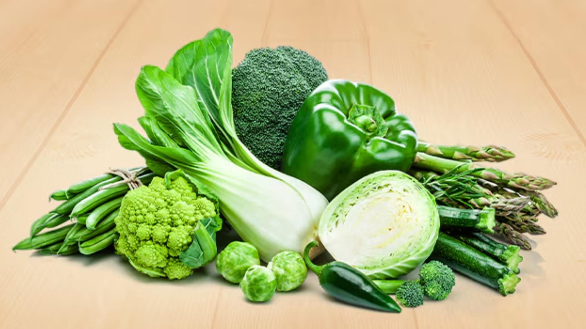 green vegetables on a wooden surface, including broccoli, bok choy, bell pepper, asparagus, and cauliflower