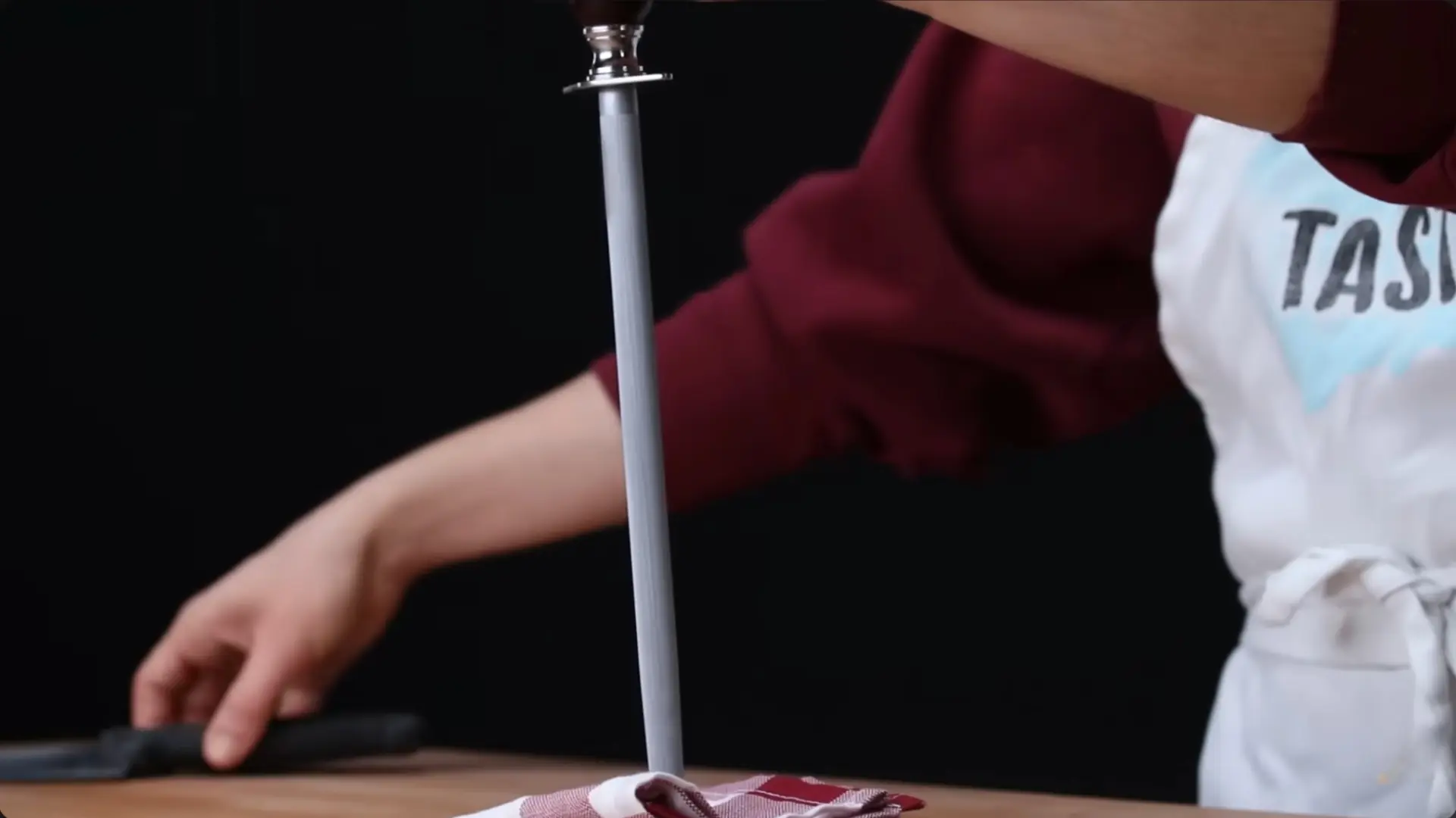 person rests a honing steel on a kitchen towel over a wooden board while preparing to sharpen a knife