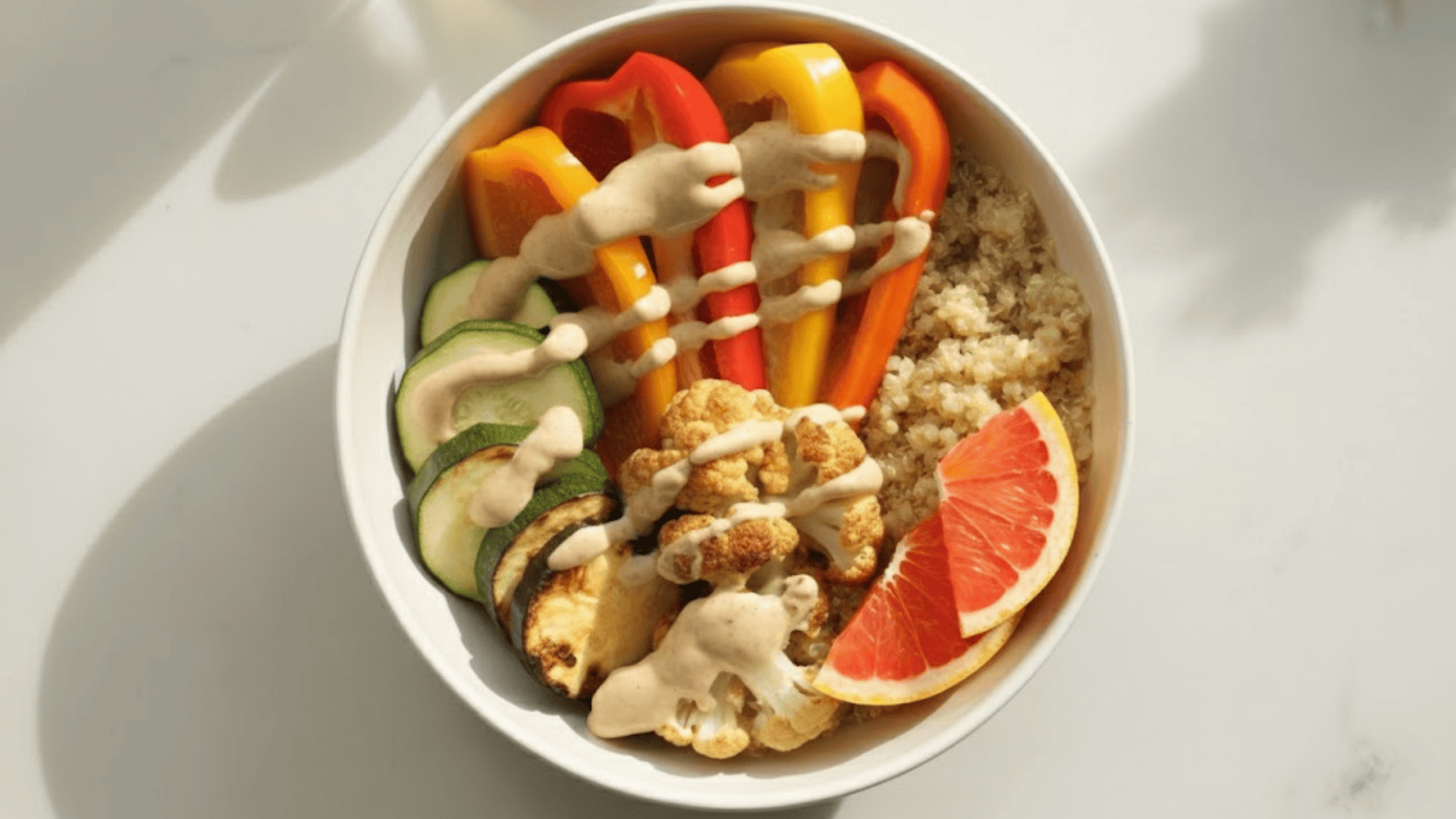 a bowl with bell peppers, zucchini, cauliflower and grapefruit over quinoa, with creamy tahini dressing