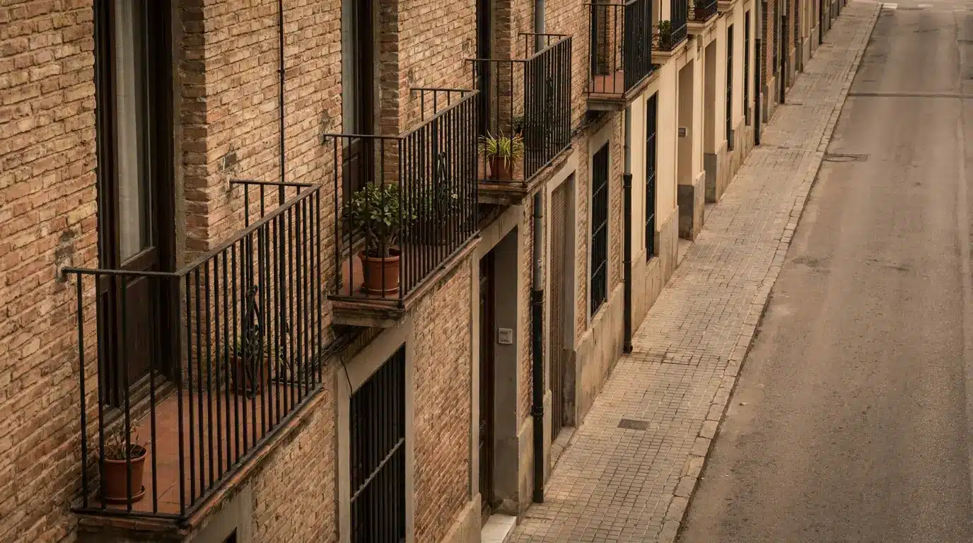 Brick apartment building with iron balconies and potted plants on a quiet street