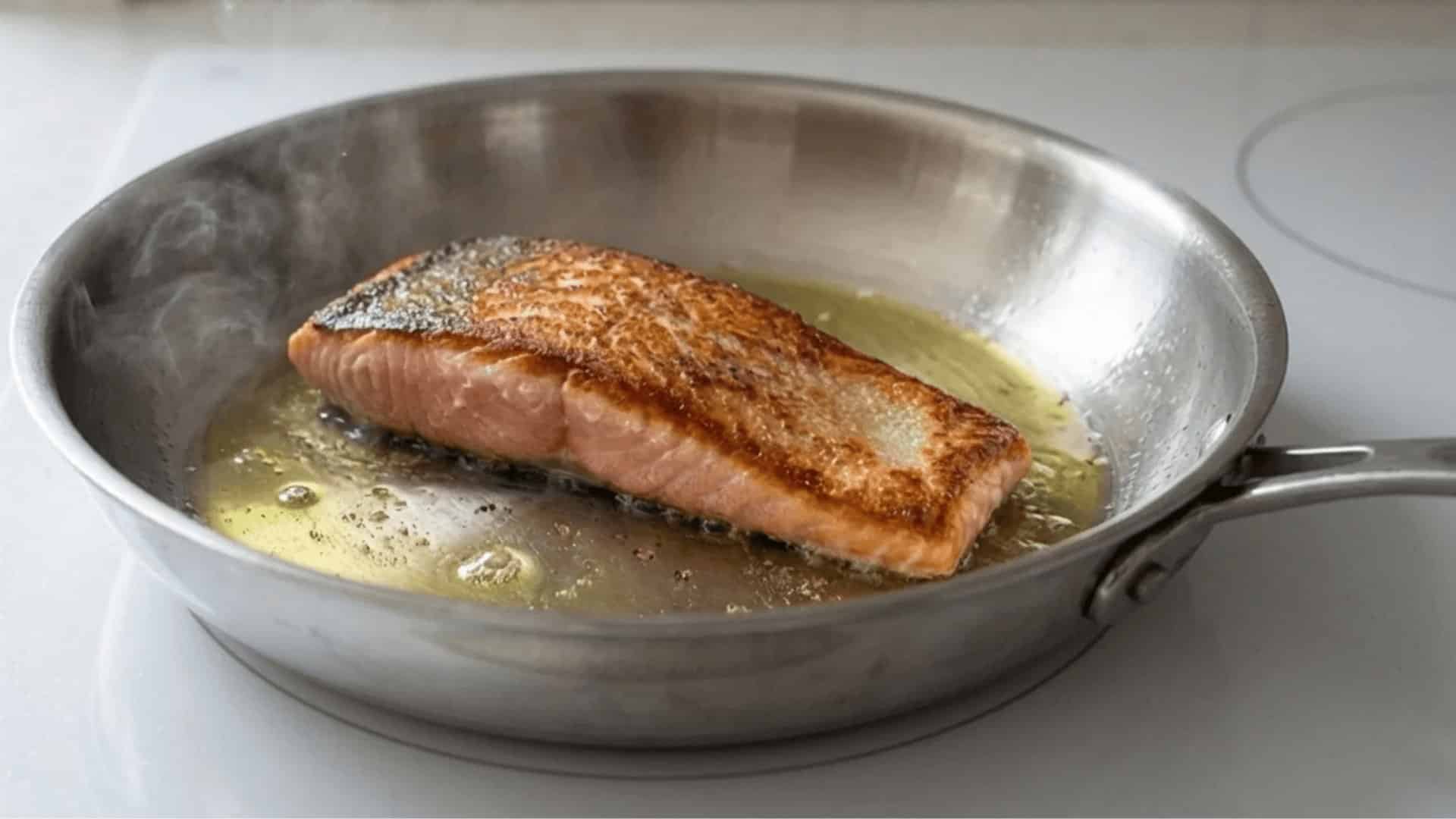 salmon fillet searing skin side down in a hot stainless steel pan with olive oil and light steam rising