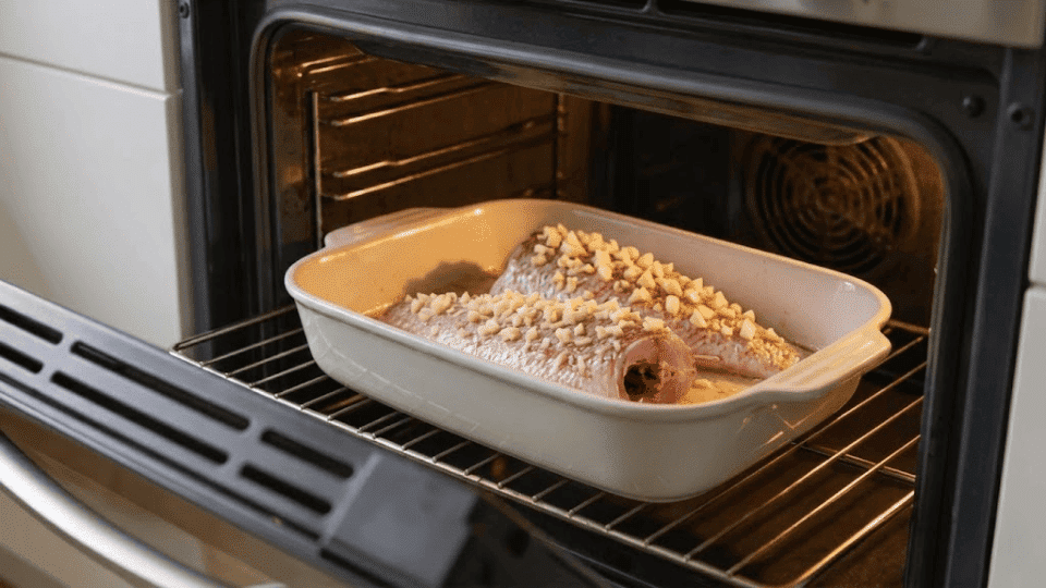 two snapper fillets baking in a white ceramic dish inside the oven turning opaque and flaking at edges