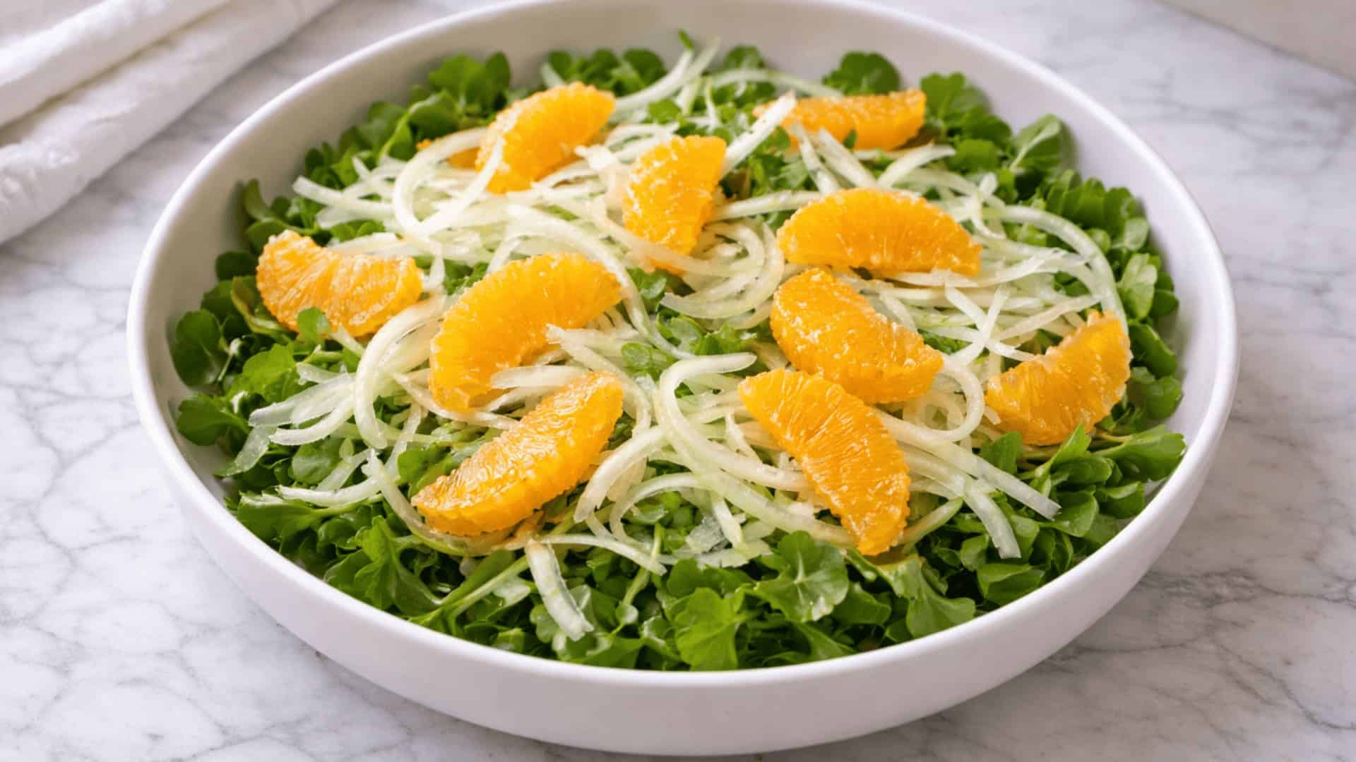 white bowl filled with fresh watercress, shaved fennel, and bright orange segments on a marble surface
