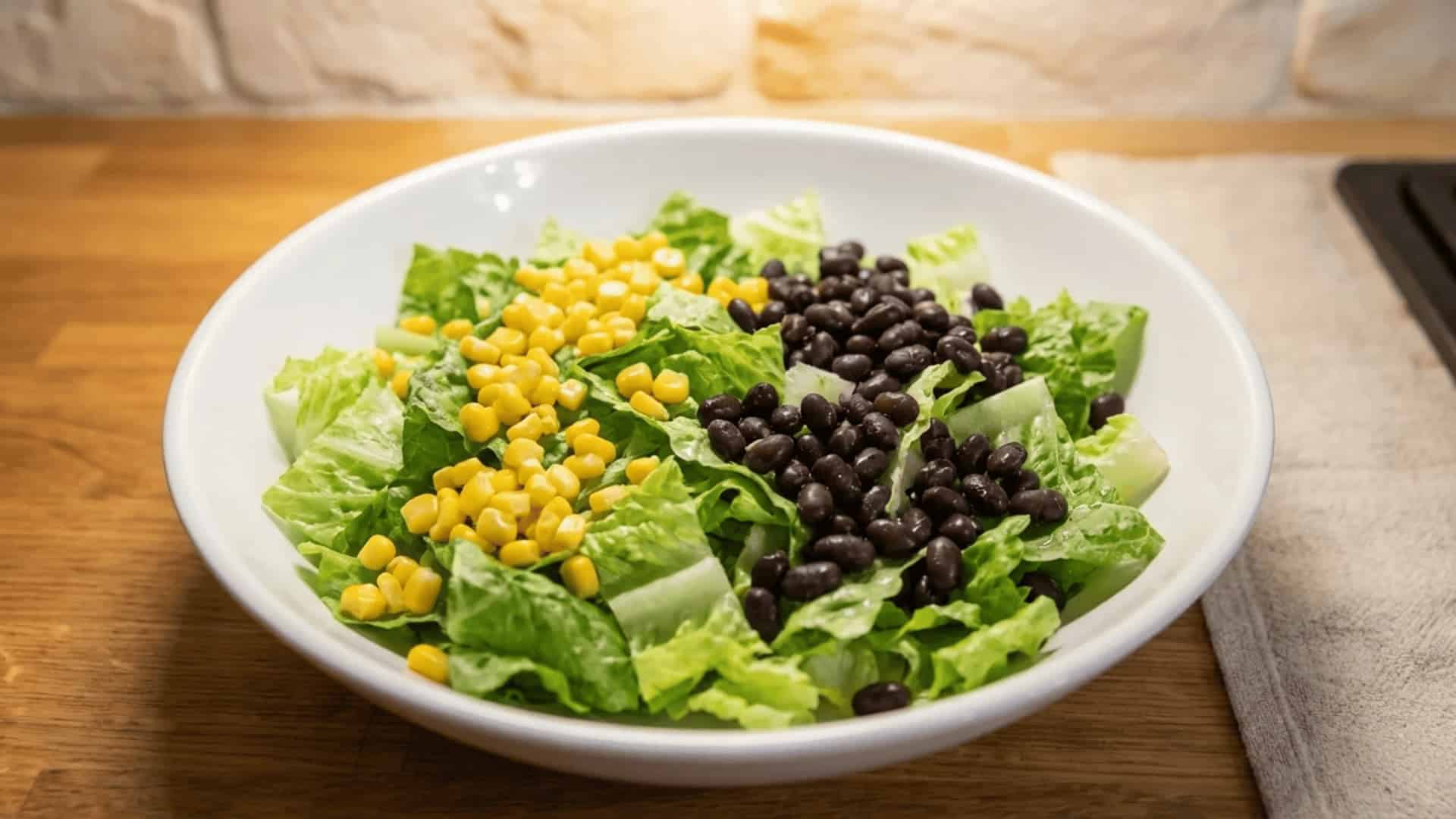 white bowl with chopped romaine lettuce topped with sweet corn kernels and black beans on a wooden surface