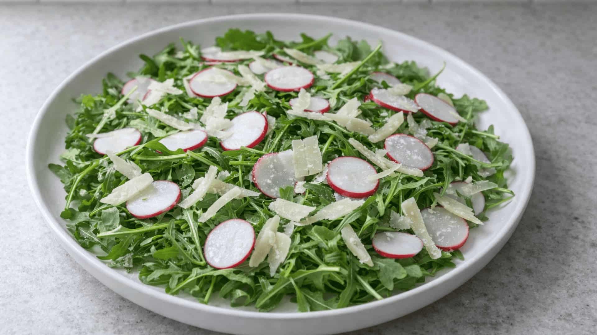 white bowl with fresh arugula salad topped with sliced radishes and shaved parmesan on a light surface