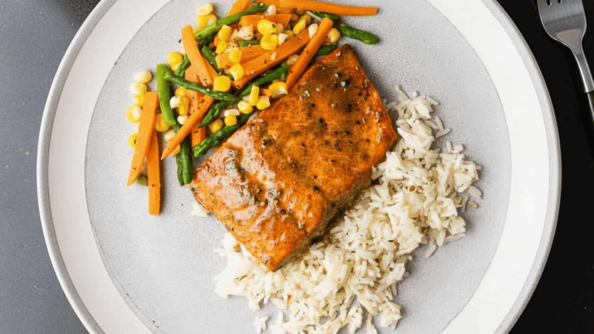 baked honey mustard salmon fillet served with white rice and sautéed vegetables on a round white plate