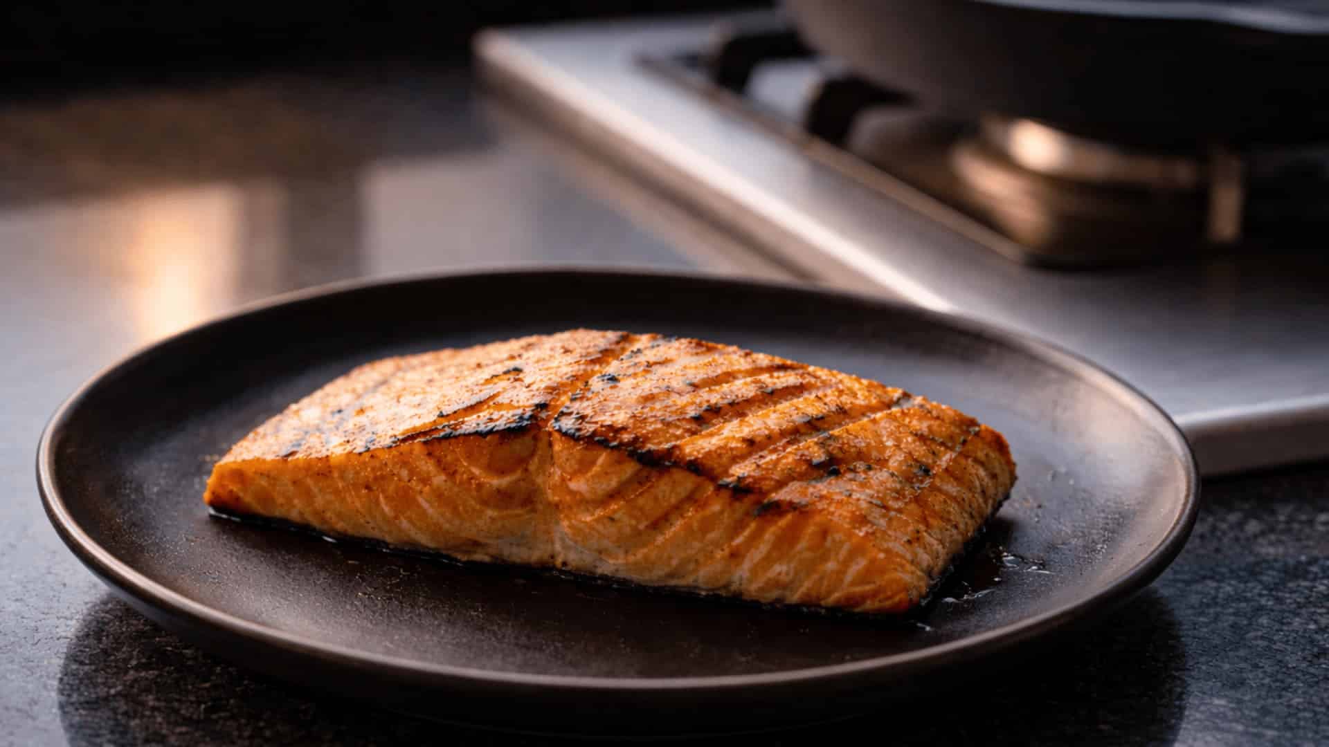 grilled salmon fillet with charred grill marks served on a dark round plate on a kitchen counter