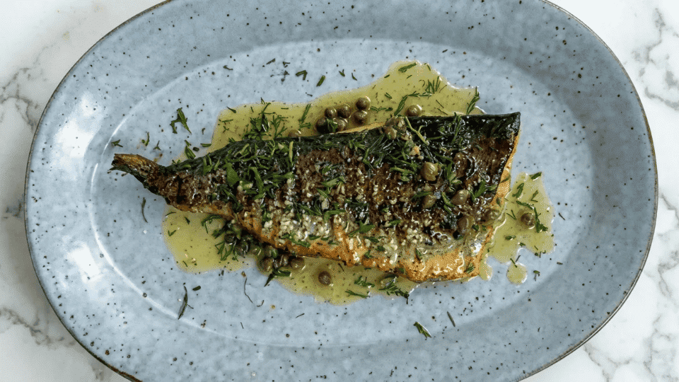 grilled trout with garlic, herbs, and capers on a plate with a lemon butter sauce