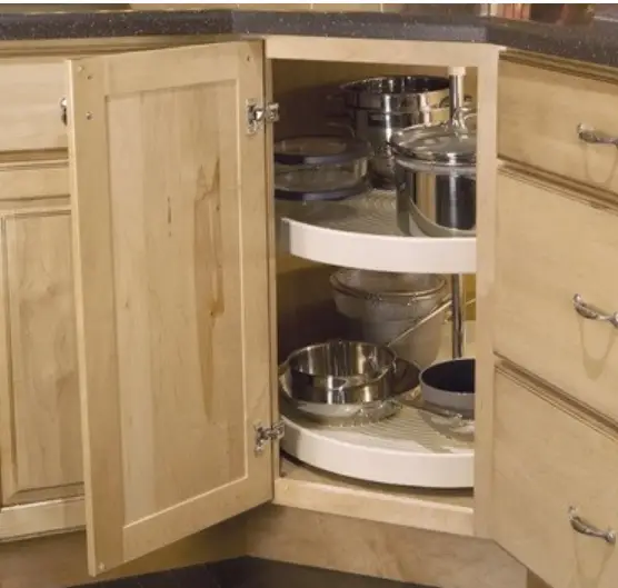 Wooden kitchen cabinet with open door revealing rotating shelves storing stainless steel pots and pans