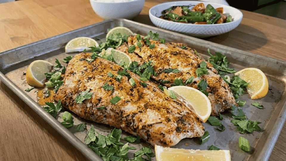 lemon garlic baked snapper with fresh herbs and lemon wedges on a baking tray