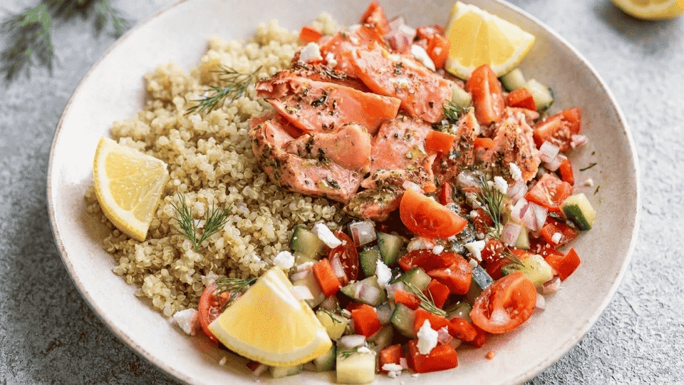 mediterranean salmon salad bowl with quinoa, fresh veggies, and lemon wedges on a plate