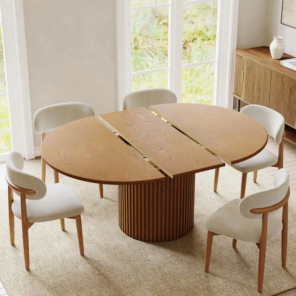 Round wooden dining table with five white cushioned chairs in a bright dining room.