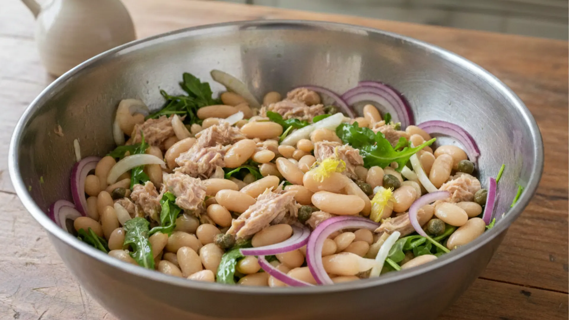 tuna and white bean salad with red onions and capers in a large metal bowl on a wooden tabletop