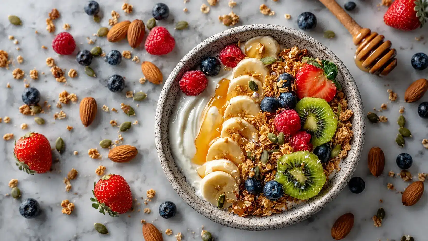 Overhead bowl of chia pudding topped with banana, kiwi, berries, granola, seeds, almonds, and honey on a marble surface