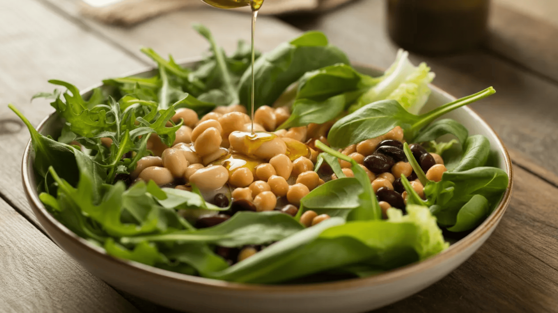 a mixed bean and leafy green salad drizzled with olive oil, served in a shallow bowl on a wooden table