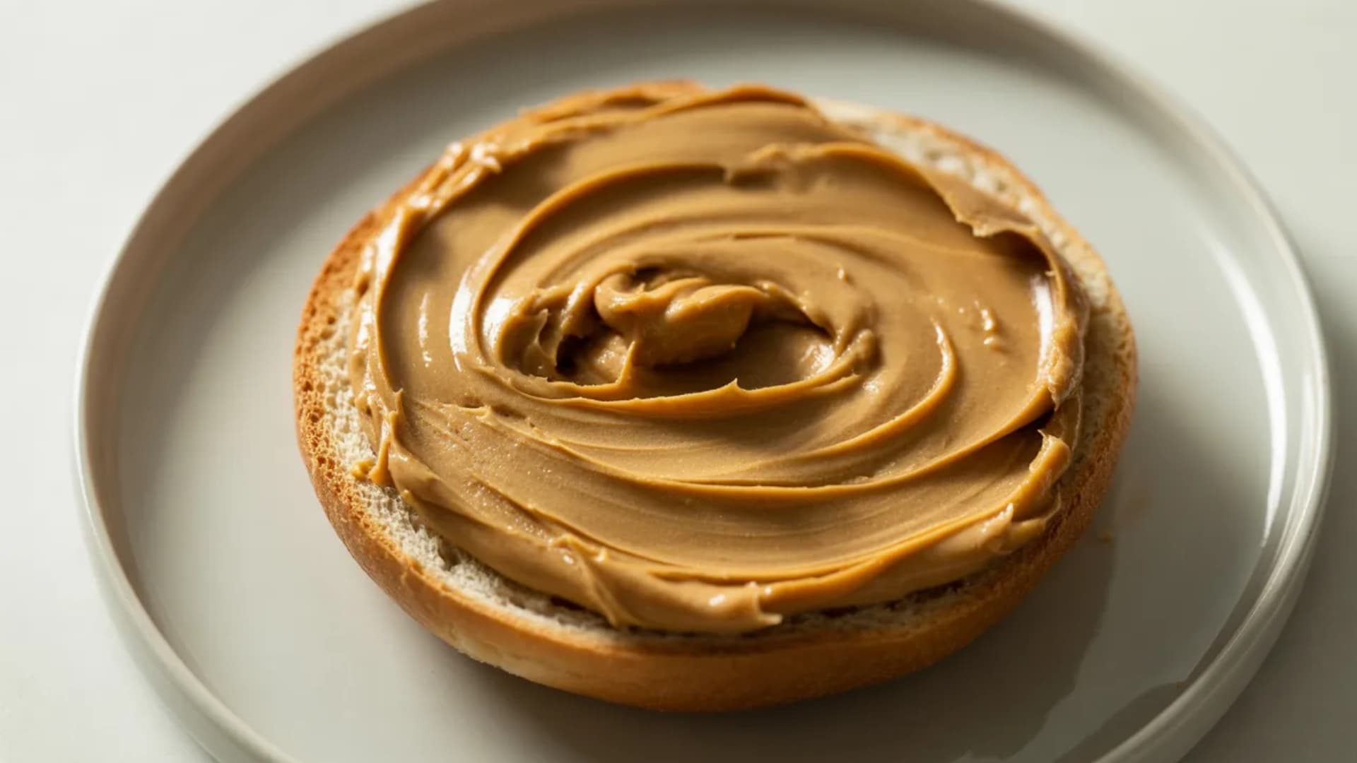 bagel half topped with thick peanut butter spread, visible texture and swirls, placed on a simple plate