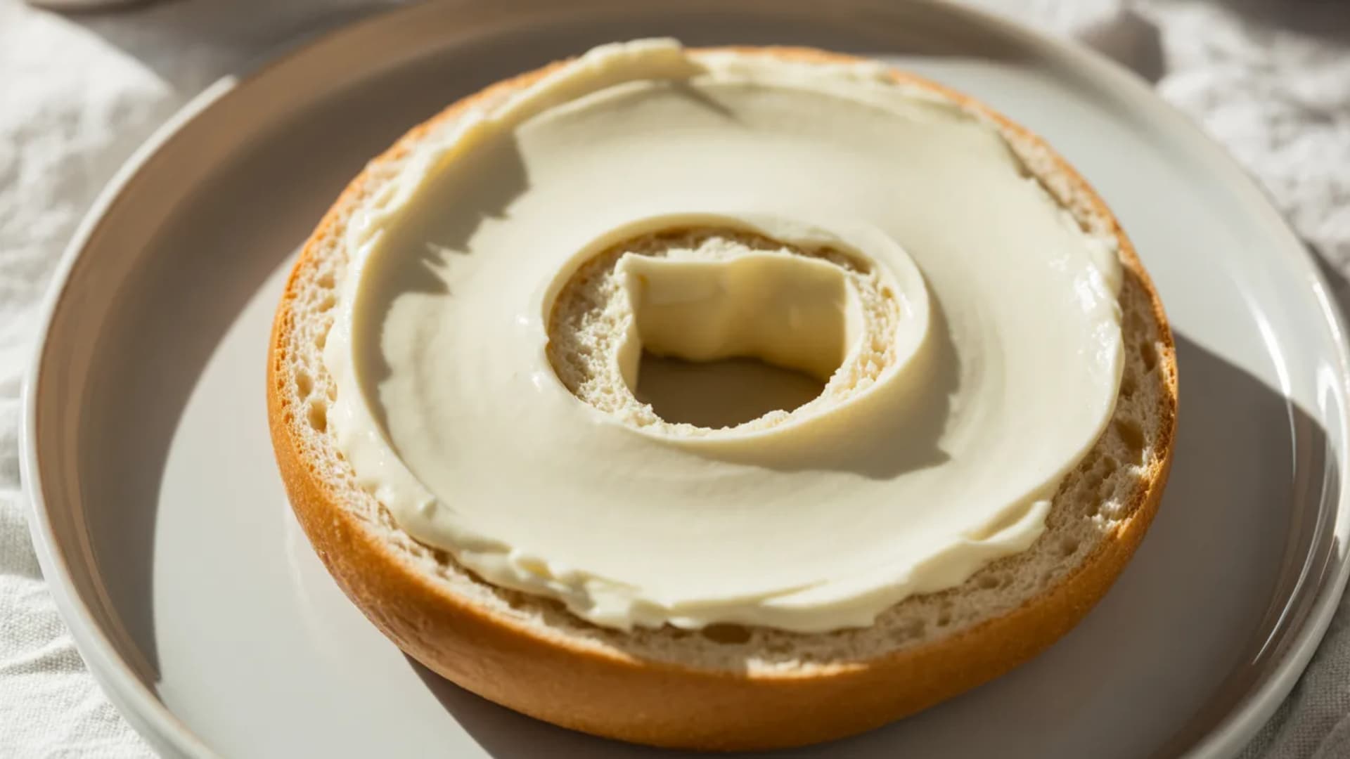 bagel sandwich with fried egg and melted cheese inside, slightly toasted bagel, warm lighting, placed on a plate, breakfast setting