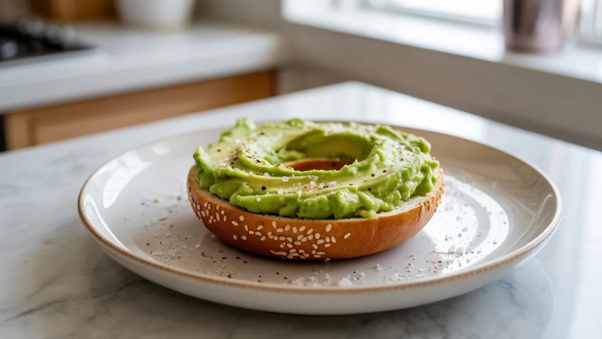 bagel topped with mashed avocado spread, light seasoning visible, fresh green color, clean plate