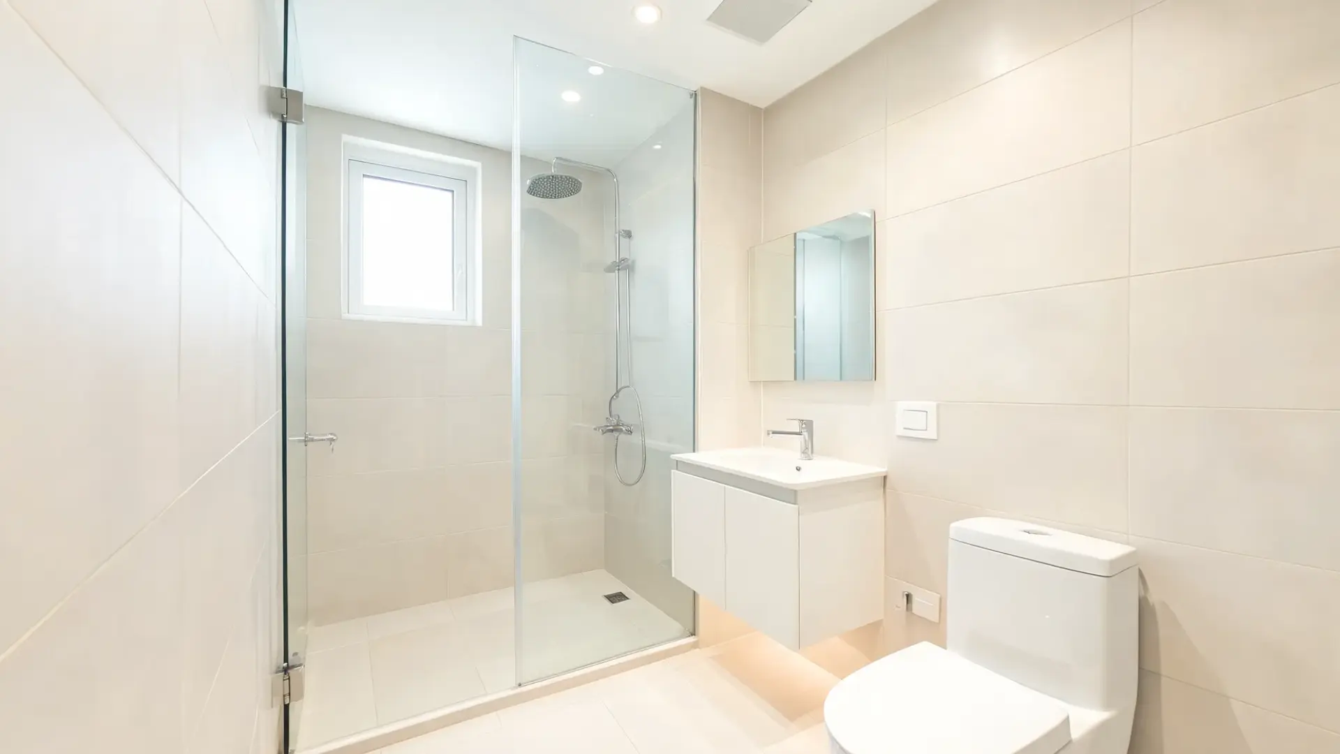 bathroom remodel featuring clear frameless glass shower doors, light tile walls, compact vanity, open sightlines