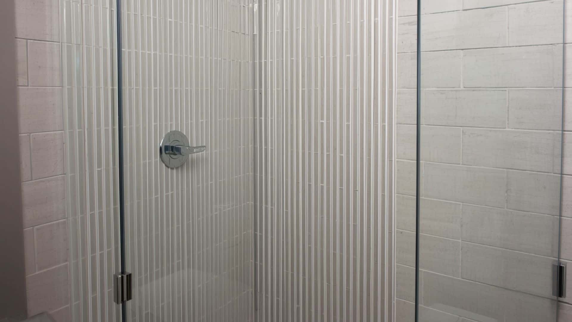 bathroom shower with vertical rectangular tiles running up the wall, clear glass shower door, slim fixtures, light grout, taller visual effect, clean modern bathroom
