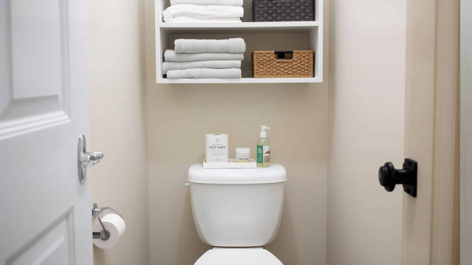 bathroom with over-the-toilet storage shelves, neatly arranged towels, baskets, and toilet paper, compact toilet, light wall color