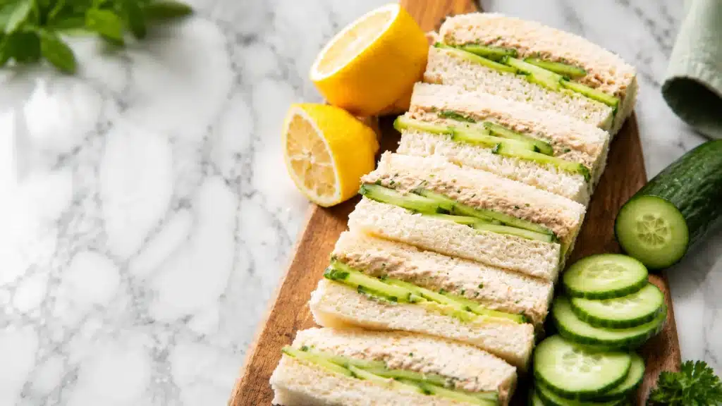 Cucumber sandwich slices with creamy filling and lemon on a wooden board, fresh healthy food close-up