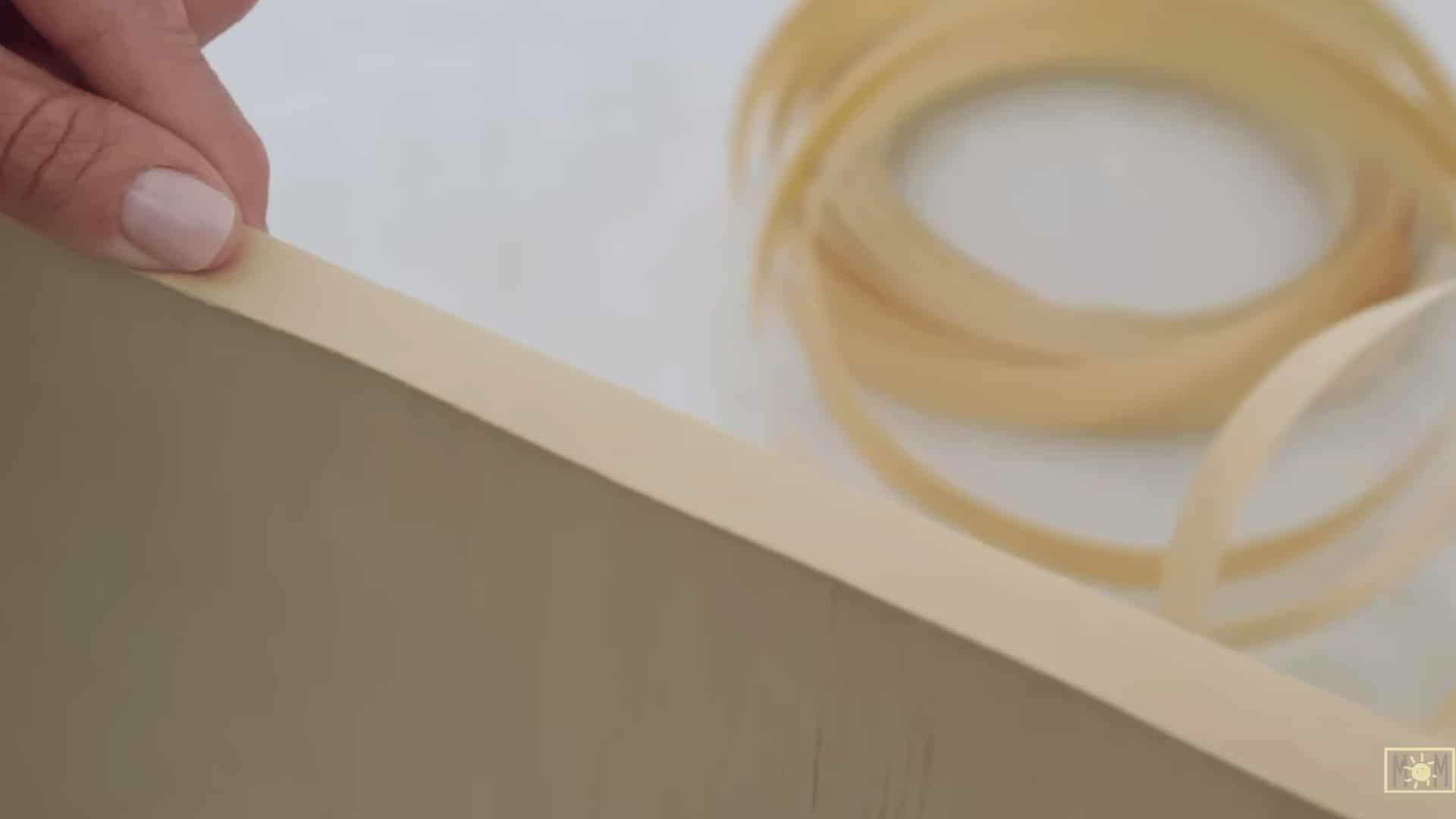 hand applying wood veneer edge banding to the exposed plywood edge while a roll of banding rests on the work surface