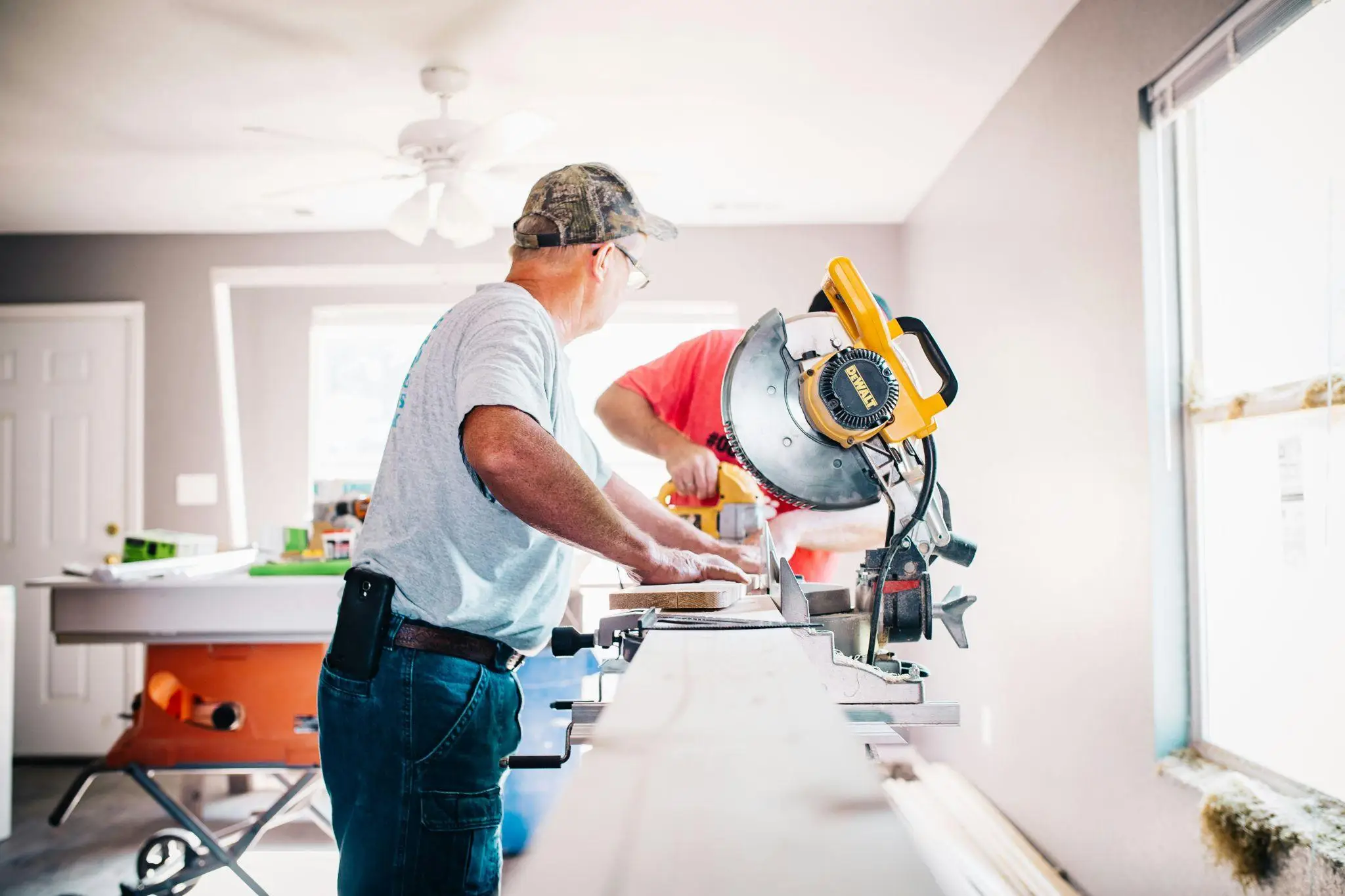 Two men working with a miter saw on wooden planks in a bright workshop
