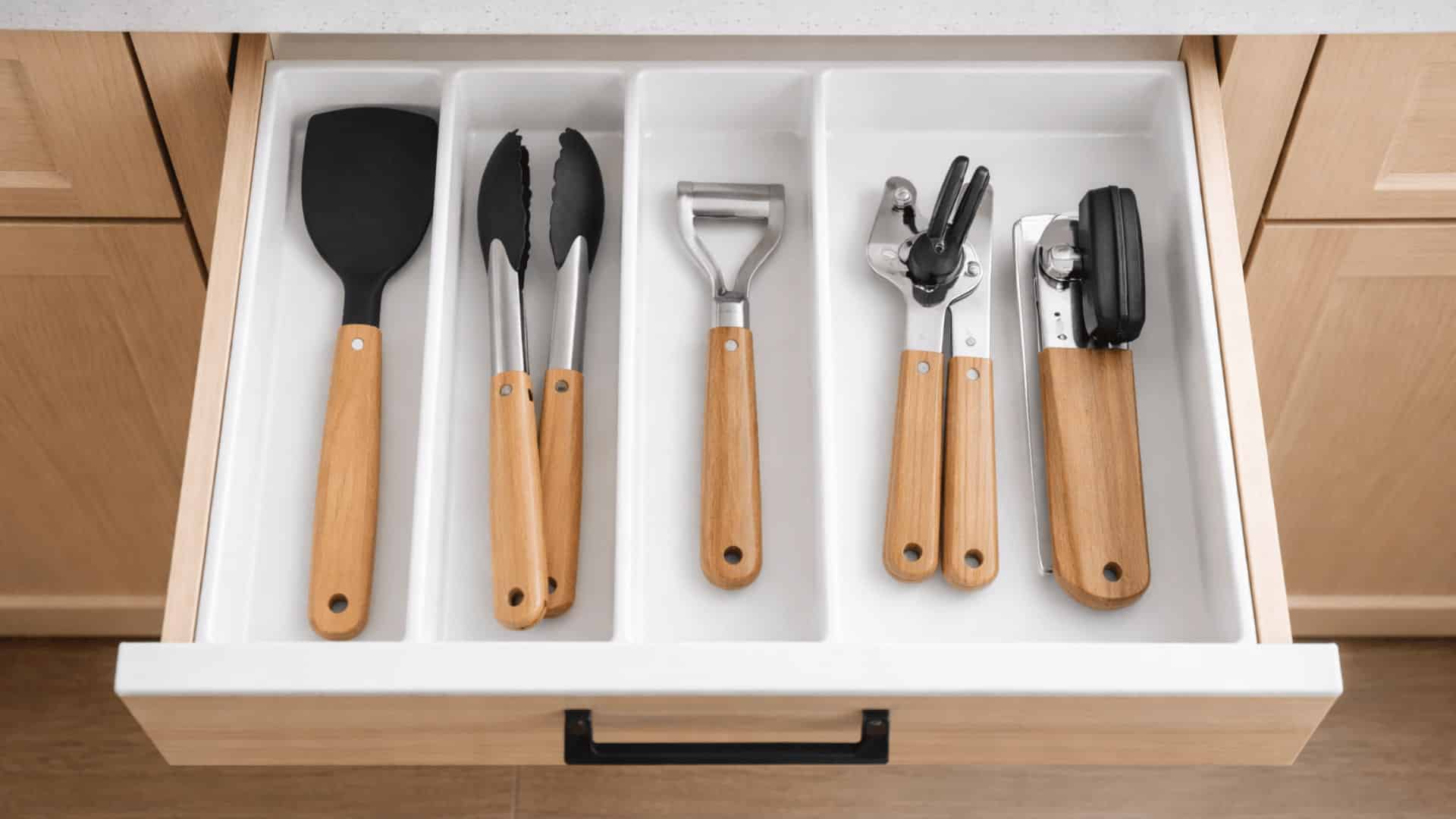 open top kitchen drawer with white organizer tray holding everyday utensils including spatula, tongs, and can opener