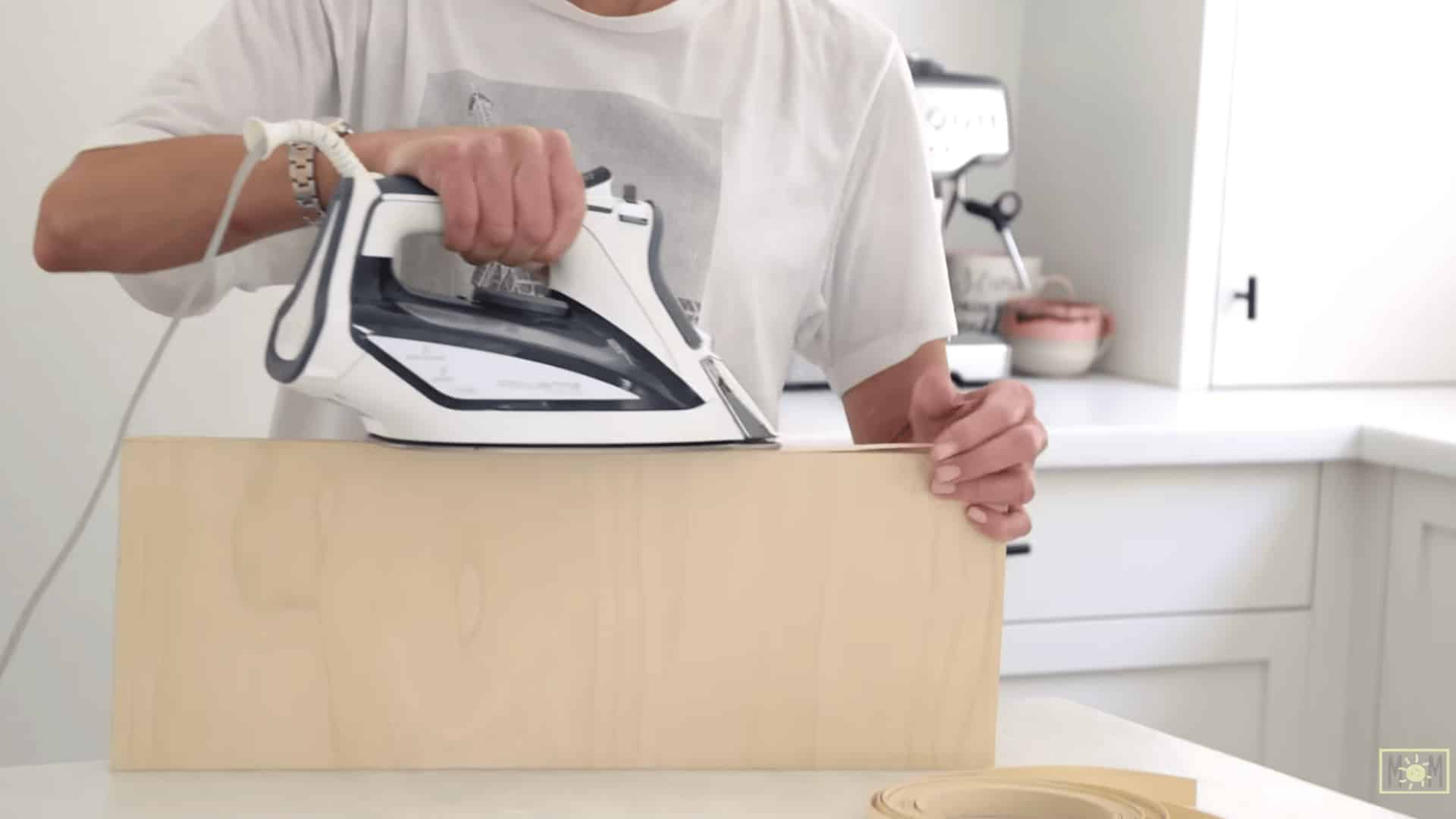 person using a warm iron to attach wood veneer edge banding to the exposed edge of a plywood divider panel
