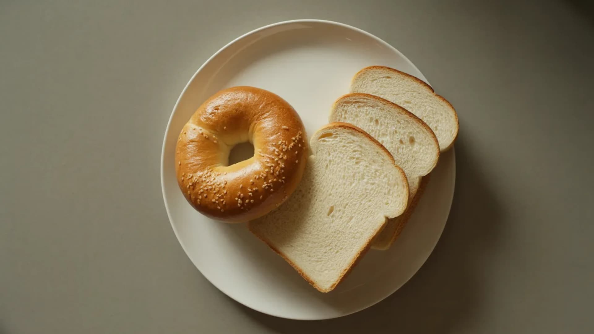 side-by-side comparison of one plain bagel and three to four slices of white bread on a clean plate